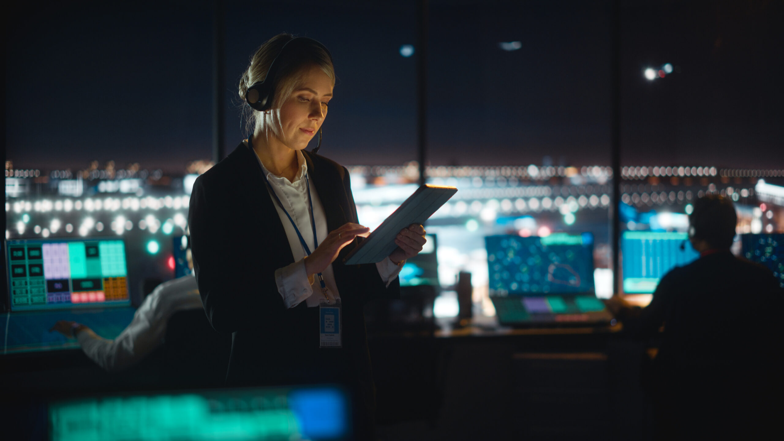 Caucasian Female Air Traffic Controller Working on Tablet in Airport Tower. Office Room is Full of Desktop Computer Displays with Navigation Screens, Airplane Flight Radar Data for the Team.
