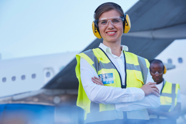 Portrait smiling female air traffic controller standing near airplane